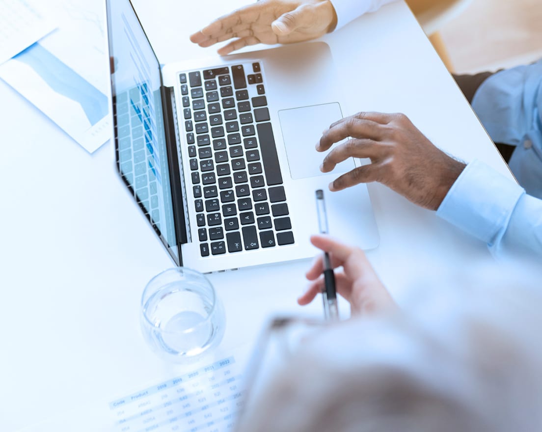 two people at a desk with a laptop and planning documents